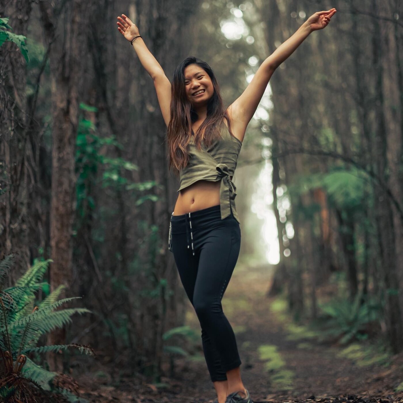 Karis with arms raised in joy on a forest path, alive between rounds of treatment